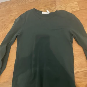 Mörkgrön långärmad tröja Weekday XS - En basic mörkgrön långärmad tröja från Weekday i storlek XS. Tröjan har rund halsringning och är gjord i mjuk bomull, perfekt för lager-på-lager eller chill vardagsstil.