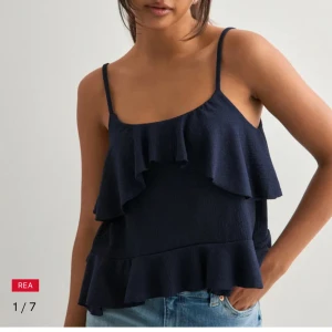 Linne från Nelly - Supersöt mörkblå linnetopp från Nelly med tunna axelband och dubbla volanger framtill och nedtill. Toppen är helt oanvänd med prislapp kvar. Säljs pga fel storlek. 