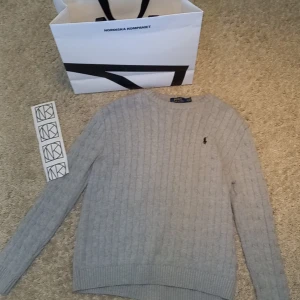Kabelstickad tröja från polo ralph lauren  - Säljer en klassisk grå stickad tröja från Polo Ralph Lauren med kabelstickat mönster och broderad logga på bröstet. Tröjan har rund halsringning och långa ärmar. Perfekt för en stilren och tidlös look. Tröjan är i storlek M så passar perfekt om du är runt 175.  Skick 8.5/10. Priset kan diskuteras vid en snabb och smidig affär. Hör av er vid minsta fråga🤗💸