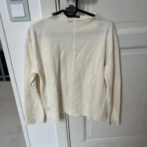Vit långärmad tröja från Zara - En stilren vit långärmad tröja från Zara i storlek S. Tröjan har en rak passform och en synlig söm mitt bak som ger en cool detalj. Perfekt att matcha med jeans eller kjol för en clean look.