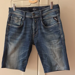Blå jeansshorts från Replay, strl 29 - Snygga blå jeansshorts från Replay i modellen Anbass. Klassisk femficksdesign med slitningar och ljusare partier för en cool, avslappnad look. Shorts med normal passform och midwaist. Perfekta för sommaren och lätta att matcha med allt.