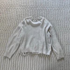 Vit stickad tröja från H&M - Supermjuk vit stickad tröja från H&M med ribbade detaljer på ärmar och hals. Tröjan har en avslappnad passform och långa ärmar. 