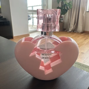 Ariana Grande parfym rosa hjärta - Superfin parfym från Ariana Grande med en rund, transparent rosa flaska och ett coolt hjärtformat rosa fodral. Flaskan har ett stilrent tryck och ett fyrkantigt lock i rosa plast. Perfekt för dig som gillar snygg design och söt doft.