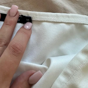 Vit bandeau tubtopp i bomull - Säljer en stilren vit bandeau tubtopp i mjuk bomull. Toppen är ärmlös och har lätt rynkade detaljer på sidorna för en snygg passform. Perfekt att matcha med jeans eller kjol för en clean look.