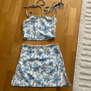 Blommigt sommar set - Superfin kortkjol i vitt med blått blommönster och liten slits på sidan med tillhörande linne som man knyter över axlarna. Passar både strl. 34 och 36