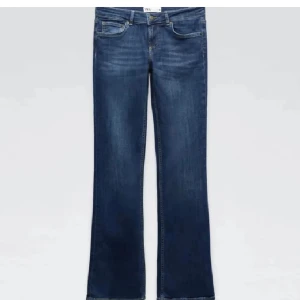 Blå bootcut jeans med normal passform - Snygga blå jeans med bootcut-snitt och klassisk femficksdesign. Jeansen har en mörk tvätt och raka ben som blir vidare nedtill. Perfekta för en avslappnad och trendig look.