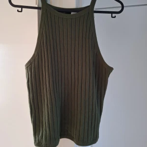 Olivgrön ribbad linnetopp H&M Divided - Säljer en olivgrön ribbad linnetopp från H&M Divided. Toppen är ärmlös med smala axelband och har en snygg, rak passform. Materialet är mjukt och stretchigt, perfekt för en chill och trendig look.