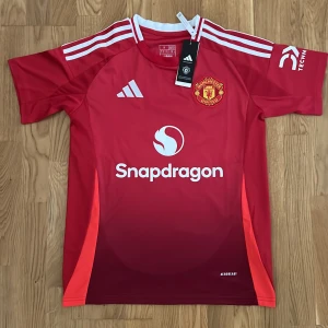 Manchester United B. Fernandes tröja S - Manchester Uniteds officiella matchtröja från Adidas i röd färg med vita detaljer och klubbmärke på bröstet. Kortärmad modell med B. Fernandes och nummer 8 på ryggen. Tillverkad i lätt funktionsmaterial med Snapdragonsponsor framtill och Aeroready-teknologi.