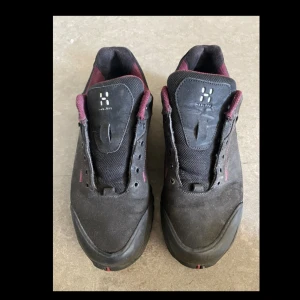 Svarta Haglöfs Ridge II GT sneakers - Svarta Haglöfs Ridge II GT sneakers med vinröda detaljer och robust sula. Skorna har ovandel i skinn och syntet, mesh på plösen och Gore-Tex-märke på sidan. Perfekta för dig som gillar outdoor och vill ha slitstarka skor.