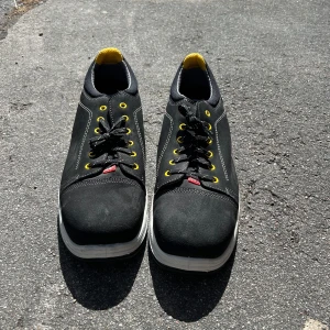 Svarta sneakers från Jalas med gula detaljer - Säljer ett par svarta sneakers från Jalas med snygga gula detaljer på insidan och vid snörhålen, den har en hård metall platta där fram men den är sköna ändå. Skorna har vit sula, svarta skosnören och  stil med en twist. Märket syns tydligt baktill. Priset går att förhandla 