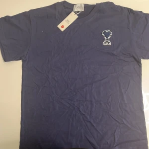 t-shirt från Ami Paris - Snygg blå t-shirt från Ami Paris med deras ikoniska hjärtformade A-logo  på bröstet. Klassisk passform med rund hals och korta ärmar. Tillverkad i mjuk bomull som känns skön mot huden. Perfekt för en clean och stilren look. Storleken är XL men passar L eller Medium bäst