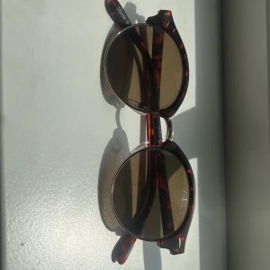 Runda solglasögon i brun sköldpaddsmönster - Snygga runda solglasögon med bruntonade glas och klassiskt sköldpaddsmönstrad båge. Metallbrygga och detaljer ger en cool vintagekänsla. Perfekta för att lyfta din stil under soliga dagar.