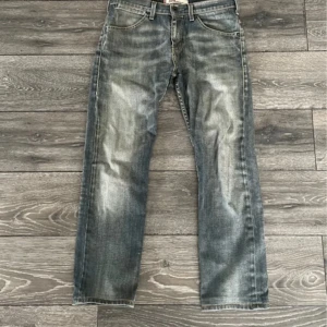 Levi's 504 straight jeans grå - Levi's 504 straight jeans i tvättad gråblå färg med slitningar. Jeansen har rak passform och normal midja. Snygga detaljer som Levi's-märke på bakfickan och metallknapp framtill.      ⭐️Jag har sytt in ett snöre så att det går att tighta till. Det finns även ett jättelitet hål på ena benet som knappt märks (se bilder) innerbenslängd: 73, W42 L99
