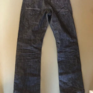 Mörkblå raka jeans - Säljer ett par klassiska mörkblå jeans med raka ben och snygga sömmar på bakfickorna. Jeansen har normal passform och är tillverkade i slitstarkt denimtyg. Perfekta för en chill och stilren look.