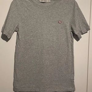 Grå t-shirt Carin Wester!  - Gråmelerad t-shirt från Carin Wester i 100% bomull. Klassisk passform med korta ärmar och rund halsringning. På bröstet finns ett broderat motiv av rosa läppar som ger en cool detalj till looken. Fint skick! Inga skador eller anmärkningar! 