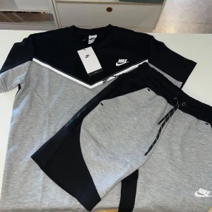 Nike grå och svart loose fit t-shirt - Nike t-shirt i loose fit med grå och svart färgblock, vit detalj och klassisk logga på bröstet. Kortärmad modell i mjuk bomull, perfekt för en sportig och avslappnad stil. Snyggt V-format mönster framtill som ger en modern vibe. Finns i alla storlekar 