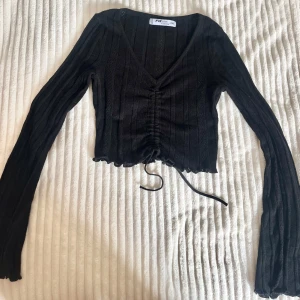 Svart croppad topp  - Snygg svart croppad topp från New Yorker med långa ärmar och jättefin ribbad struktur. Toppen går att justera där framme ifall man vill ändra form och göra kortare, tröjan är även redan croppad så tänk på de. Jättefin tröja nu till sommaren passa på💗