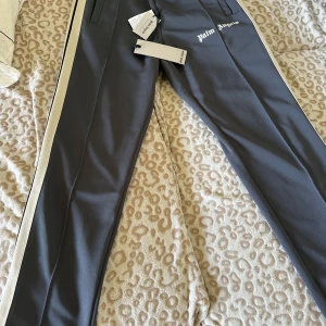 Palm Angels byxor - Dark grey/Off white - Äkta palm angels byxor, som bara är använda ett fåtal gånger. En av de bästa modellerna på marknaden. Skick 9/10 Hör av er vid frågor eller bud.