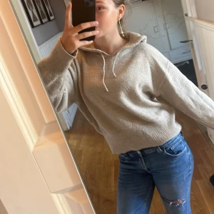 Beige stickad hoodie  - Mysig beige stickad hoodie med huva och snörning. Tröjan har en loose passform, ribbade muddar och är långärmad. Perfekt för lager-på-lager och chill dagar.