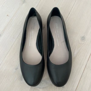 Svarta ballerinaskor från ECCO - Stilrena svarta ballerinaskor från ECCO i mjukt skinn. Skorna har rund tå, platt sula och klassisk design som passar till många outfits. Sparsamt använda. 