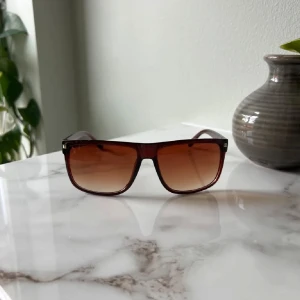 Bruna fyrkantiga solglasögon - Snygga solglasögon med fyrkantig form och brunt transparent plastbåge. Glasen är tonade i brunt och ger en cool retrovibe. Perfekta för att lyfta din stil under soliga dagar.