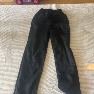 Svarta mjukisbyxor med resårmidja - Svarta mjukisbyxor med rak passform och elastisk midja. Perfekta för chill dagar eller när du vill vara extra bekväm. Tillverkade i mjukt material som känns skönt mot huden.