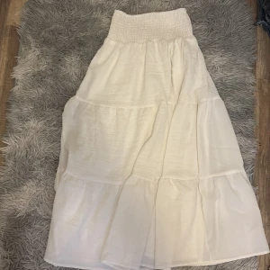 Vit långkjol från SHEIN XS - Superfin vit långkjol från SHEIN i storlek XS. Kjolen har smockad midja och flera volanger som ger en flowy och luftig känsla. Tillverkad i ett lätt och skönt polyestertyg, perfekt för varma dagar. Enkel att matcha med crop tops eller stickade tröjor.