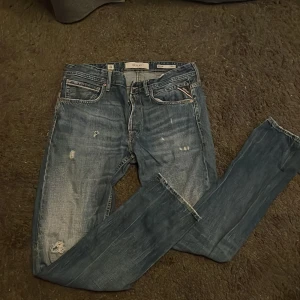 Replay - Säljer ett par blå Replay jeans med snygga slitningar och distressed detaljer. Klassisk femficksmodell med dragkedja och raka ben. Jeansen har en cool tvättad look och passar perfekt till sneakers eller boots.