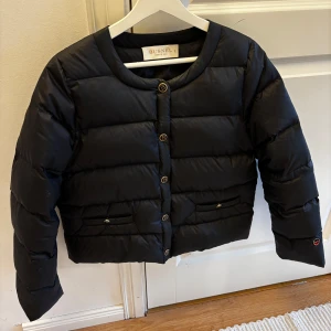 BUSNEL Ingrid down jacket - Snygg svart jacka från Busnel med rund halsringning och guldiga knappar med B-logga. Jackan är inköpt 2023 och använd endast ett fåtal gånger. Nypris ca 6000 kr.