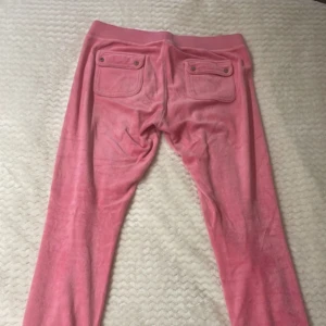 Rosa vintage Juicy Couture set - Säljer ett par klassiska rosa mjukisbyxor från Juicy Couture i mjuk velour samt matchande koftan till. Byxorna har resår och snörning i midjan samt muddar vid bensluten. Innehåller tröja med dragkedja och matchande byxor. Perfekta för en chill och trendig look. 
