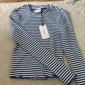 Randig långärmad tröja från Grunt - Superfin ribbad långärmad tröja från Grunt i blått och vitt randigt mönster. Tröjan har en tight passform, rund halsringning och vågig kant nertill för en extra snygg detalj. Perfekt att styla med jeans eller kjol. Nypris är 400kr