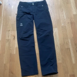 Svarta friluftsbyxor från Haglöfs - Säljer ett par svarta friluftsbyxor från Haglöfs med raka ben och dragkedjor vid fickorna. Perfekta för utomhusaktiviteter och har en stilren design med logga på låret. Byxorna har normal passform och är tillverkade i syntetmaterial.