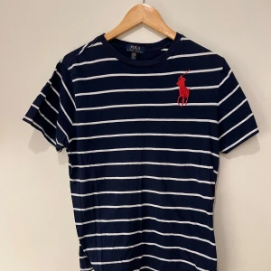 Polo Ralph Lauren Big Pony  - Säljer en snygg mörkblå Polo Ralph Lauren t shirt med vita horisontella linjer och en röd Ralph Lauren logga. Den har en klassisk Big Pony deisgn som är sälsynt att köpa. Den är i mycket bra skick och funkar som ny, sälja p.g.a den inte kommer till anövming mer 