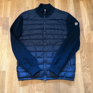 Moncler cardigan - Snygg mörkblå dunväst med ärmar från Moncler. Köpt här på plick. Västen har quiltad framsida, dragkedja och Moncler-logga på ärmen. Perfekt för lager-på-lager och har en sportig men stilren look. Den är använd varsamt under hösten förra året och tidig vår. Om ni har några frågor är det bara att skicka ett DM.