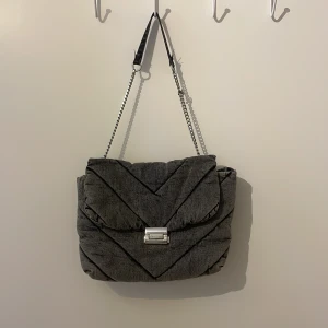 Grå väska från zara - Säljer en snygg grå quiltad axelväska från zara med silverfärgat spänne och kedjedetaljer på remmen. Väskan har ett stort huvudfack och innerficka. Perfekt för dig som vill ha en trendig och rymlig väska till vardagen. 