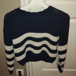 Mörkblå och vit stickad tröja från Lindex - Säljer en stickad tröja från Lindex i mörkblått med vita vågiga ränder. Tröjan har långa ärmar och ribbstickad hals, ärmslut och nederkant. Perfekt för kyligare dagar. Tröjan är i ett jätte bra skick 