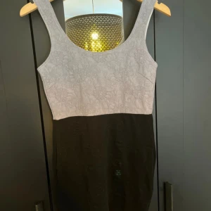 Tvåfärgad klänning med blommönster - Säljer en snygg klänning med ljusgrå överdel med blommigt mönster och svart, tight kjoldel. Ärmlös modell med rund halsringning. Perfekt för dig som gillar stilrena kontraster och enkel design.