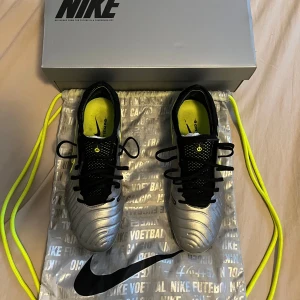 Nike tiempo legend storlek 42 elite  - Säljer ett par Nike fotbollsskor i silver med svarta och neongula detaljer. Skorna har snörning och rund tå, samt dobbar för spel på gräs. Snygg design med Nike-logga på sidan och insida. Perfekt för dig som vill sticka ut på planen!