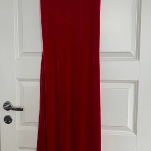 Röd långklänning i sammet - Säljer en röd långklänning i mjuk sammet med breda axelband och rundad halsringning. Klänningen har en elegant och enkel design som ger ett stilrent intryck. Perfekt för dig som vill sticka ut med en klassisk look.