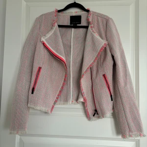 Ljusrosa kavajjacka från Amisu - Säljer en ljusrosa kavajjacka från Amisu i vävt tyg med fransade kanter och svarta dragkedjor. Jackan har en öppen front och detaljer i rosa och vitt. Perfekt för dig som gillar en chic och trendig stil.