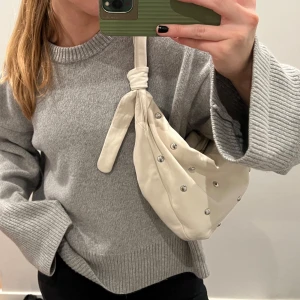 Maje väska  - Säljer en vit väska från maje  med coola silvriga nitar och knutdetaljer på axelbandet. Väskan går att knyta på olika sätt!