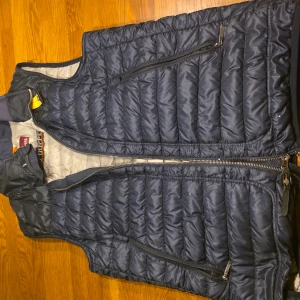Mörkblå dunväst från Parajumpers - Säljer en mörkblå quiltad dunväst från Parajumpers med dragkedja framtill och två snedställda fickor med dragkedja. Västen har en klassisk passform och är perfekt för lager-på-lager under kyliga dagar.