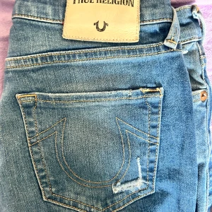 Blå True Religion jeans HALLE - Säljer ett par blå True Religion HALLE jeans med klassisk broderad bakficka och snygga kontrastsömmar. Modellen är super skinny med mellanmidja och stretchigt material för en bekväm passform.