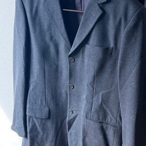 Mörkgrå kavaj från Steel - Säljer en stilren mörkgrå kavaj från Steel med tre knappar framtill och klassiska fickor. Kavajen är tillverkad i en blandning av polyester och ull, vilket ger en snygg och bekväm passform. Perfekt för dig som vill ha en tidlös look. vintage kavaj från märket Steel, köpt på en second hand butik i Köpenhamn  