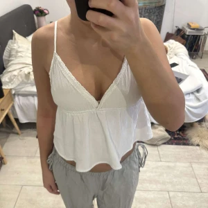 Vit croppad linnetopp med tunna axelband - Säljer en vit croppad linnetopp med tunna axelband och v-ringning. Toppen har en lös passform och lätt volang nedtill, perfekt för varma dagar. Ik zara