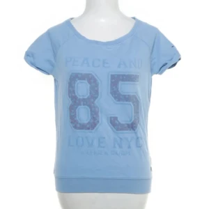 Ljusblå t-shirt med tryck från Lexington - Ljusblå t-shirt med stort tryck '85' och texten 'Peace and Love NYC' framtill. T-shirten har korta ärmar och rund halsringning. Perfekt för en avslappnad och sportig stil.