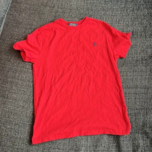 Röd t-shirt från Polo Ralph Lauren - Säljer en klassisk röd t-shirt från Polo Ralph Lauren med liten broderad logga på bröstet. T-shirten har rund hals och korta ärmar. Perfekt basic-plagg för garderoben.