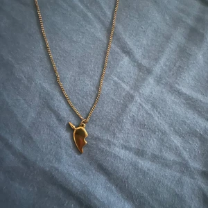 Guldigt halsband med hjärthänge - Säljer ett stilrent halsband i guld med ett unikt hjärthänge som har en delad design. Perfekt för dig som vill ha ett personligt smycke som sticker ut lite extra.