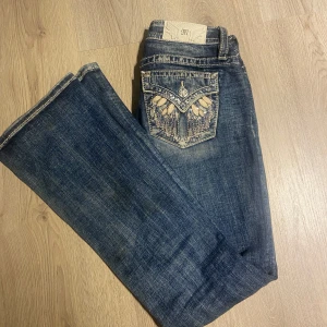 Mörkblå jeans med broderad bakficka från Miss Me - Säljer ett par snygga mörkblå jeans från Miss Me med broderade detaljer och paljetter på bakfickan. Jeansen har låg midja och är utsvängda- högsta budet gäller!