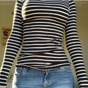 Svartvit randig långärmad tröja - Säljer en svart och vit randig långärmad tröja med tight passform. Tröjan har rund halsringning och är tillverkad i ett mjukt, stretchigt material som sitter snyggt på kroppen. Perfekt till jeans eller kjol!